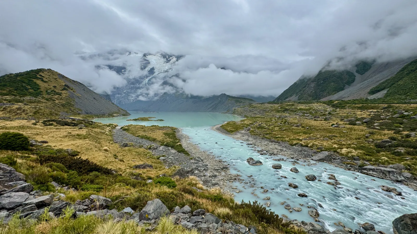 Mueller Lake and its turquoise glacial outflow on a cloudy day at Aoraki/Mount Cook.